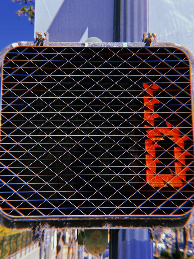 Red pedestrian countdown number 1 illuminated behind a black geometric protective grid on a crossing signal in San Francisco.