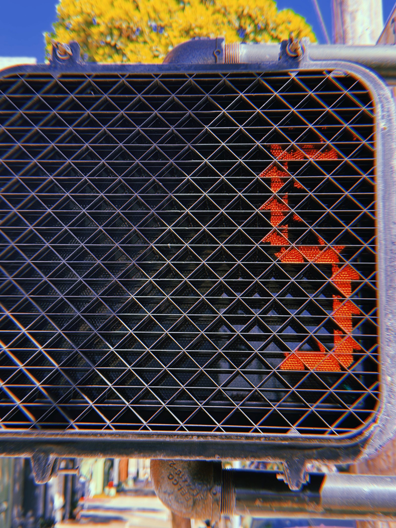 Close-up of a red pedestrian countdown number 7 illuminated behind a black geometric protective grid on a crossing signal in San Francisco.