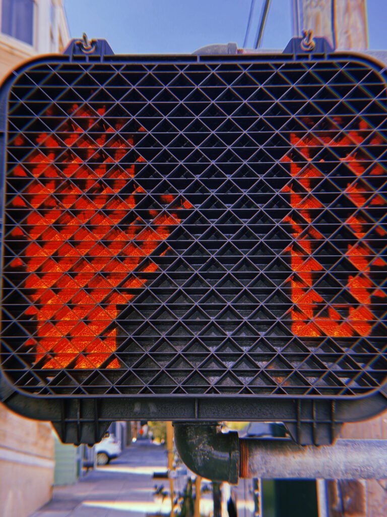 Two illuminated red pedestrian stop-hand symbols behind a black protective grid on a pedestrian crossing signal in San Francisco.