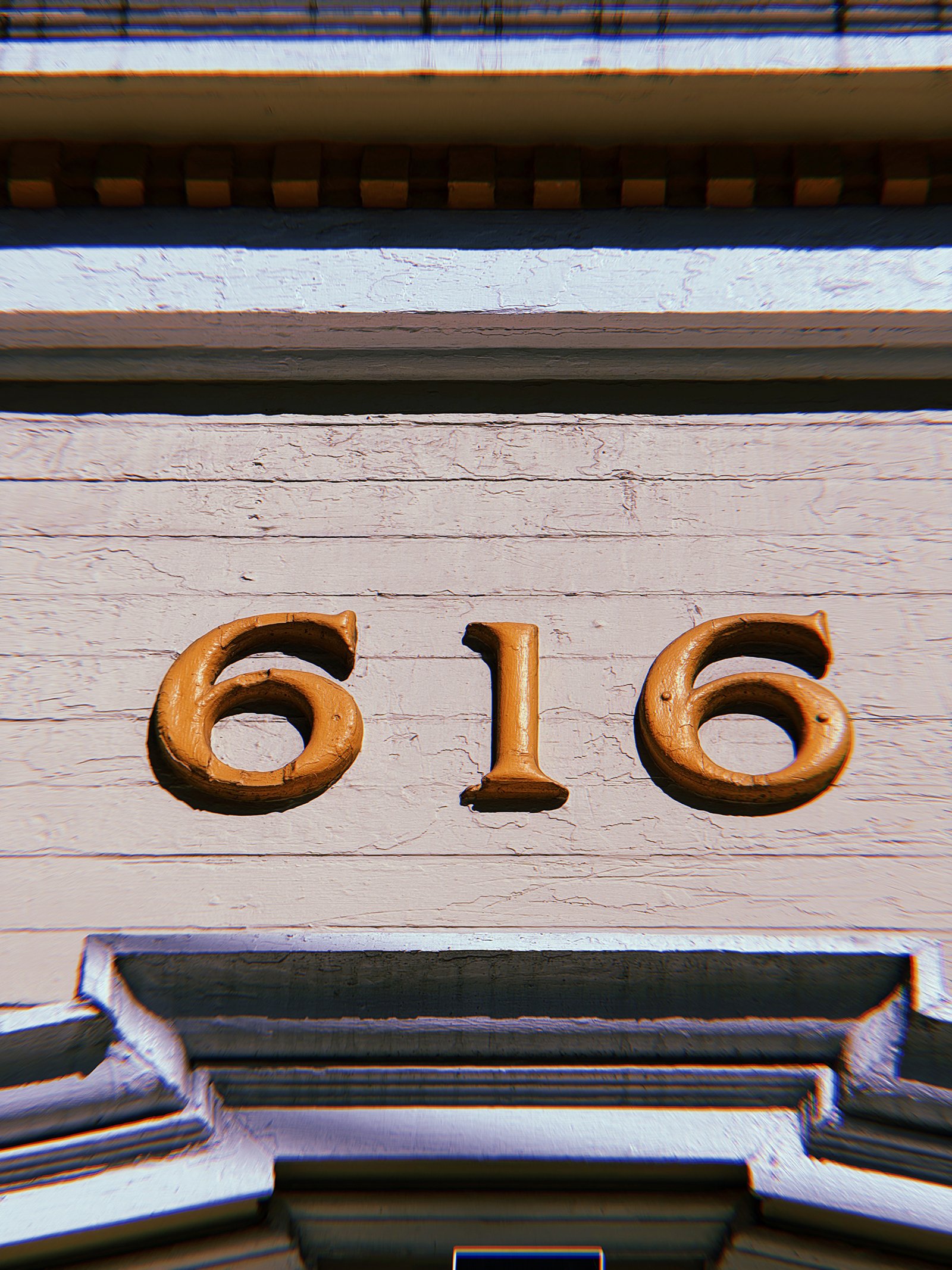 Gold address numbers 616 mounted horizontally on a weathered white wooden facade above an entrance with decorative architectural molding.