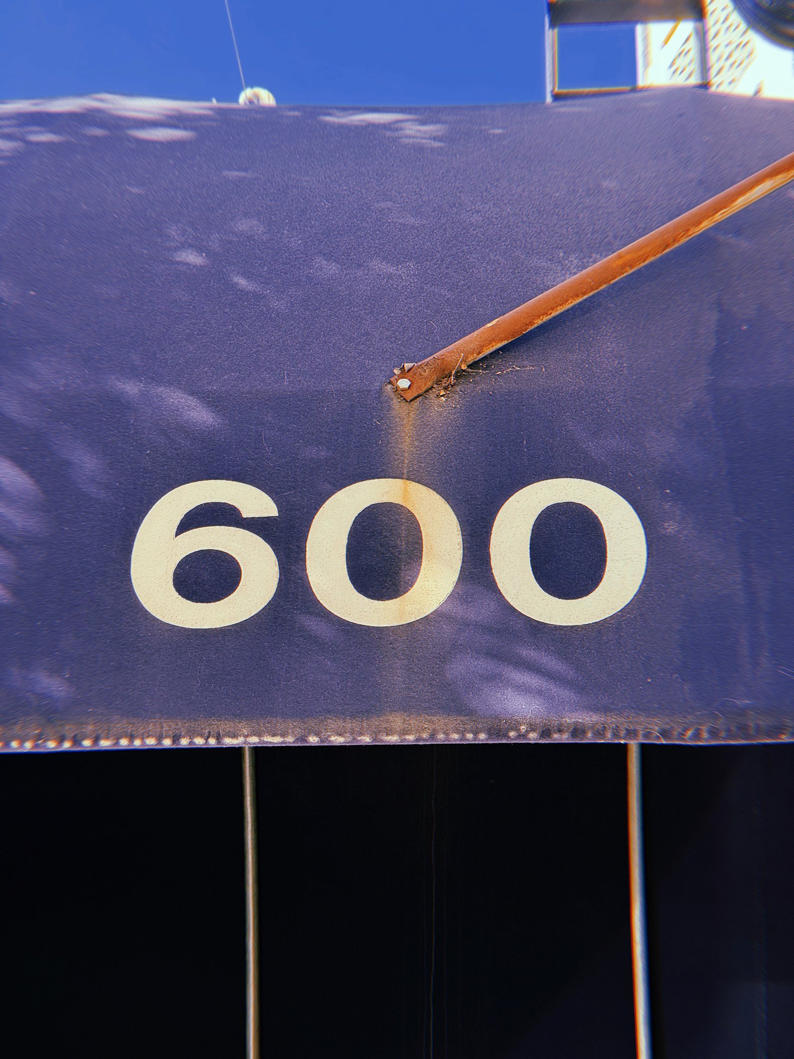 Large cream-colored address numbers 600 printed on a weathered dark blue awning, with a diagonal rust-colored metal support above.