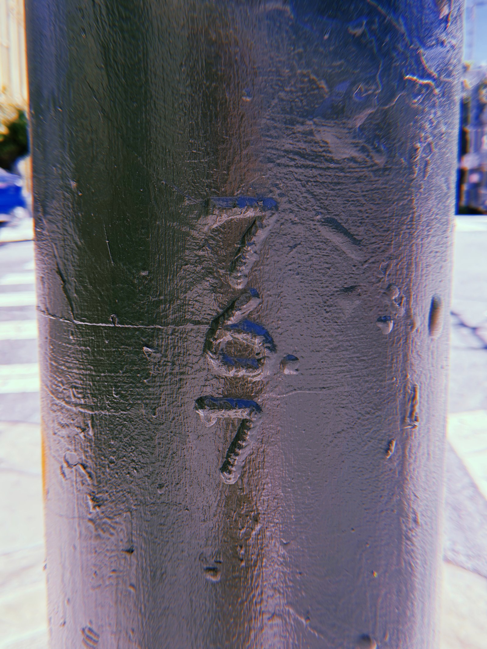 Vertical numbers 267 embossed into a dark-painted metal utility pole at a San Francisco street intersection, partially obscured by layers of paint.